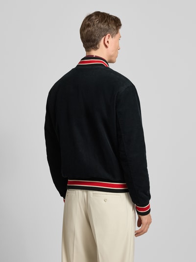 Männermodel trägt College-Jacke aus Cord mit Label-Detail von Gant in Schwarz, Regular-Fit, reine Baumwolle, Stehkragen, Rückansicht, Herrenjacke, Knopfleiste, Eingrifftaschen, Rückenlänge 66 cm, Schulterbreite 46 cm, Brustweite 53 cm, Ärmellänge 67 cm, Struktur und Farbakzente sichtbar, Ganzkörperansicht Rückansicht.