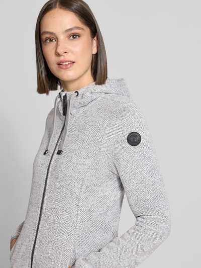 Frauenmodel trägt Regular Fit Sweatjacke mit Logo-Detail von G.I.G.A. DX in hellgrau melierter Textur, Reißverschluss, Kapuze, Eingrifftaschen, Nahaufnahme Oberkörper. Rückenlänge, Schulter- und Brustweite sowie Ärmellänge entsprechen Größe 36.