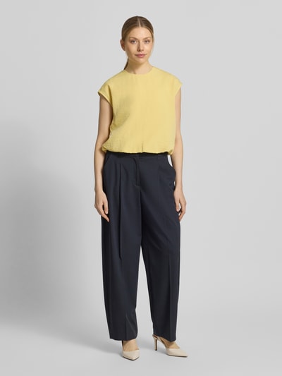 Frauenmodel trägt Bluse mit Rundhalsausschnitt und Kappärmeln von Jake*s Collection in Gelb, strukturierte Oberfläche, kombiniert mit dunkelblauer Stoffhose, Ganzkörperansicht von vorne.