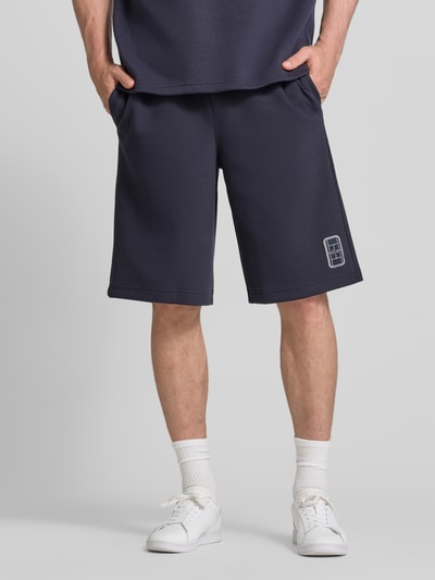 Mannenmodel draagt Relaxed Fit Sweatshorts uit katoenmix van Lacoste in donkerblauw, gladde textuur, heren sweatshorts, detailopname benen.