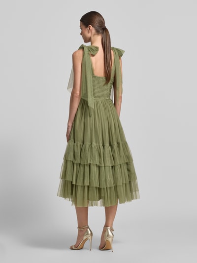 Frauenmodel trägt Knielanges Kleid mit Rüschenbesatz von LACE & BEADS aus olivgrünem Mesh, taillierter Passform, Zierschleifen, Ärmelloses-Design, Knielänge, Rückenlänge bei Größe S 117 cm, Brustweite 32 cm, Ganzkörperansicht Rückansicht.