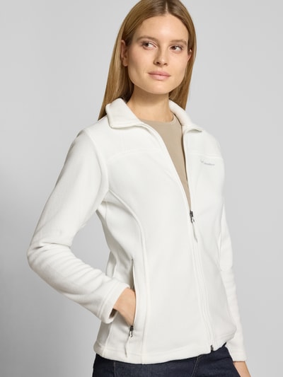 Frauenmodel trägt Slim Fit Fleecejacke mit Ärmeltasche Modell 'Fast Trek™ II' von Columbia in Weiß mit Stehkragen, Reißverschlusstaschen und Label-Detail, Fleece, elastische Abschlüsse, Ganzkörperansicht von vorne. Rückenlänge 63 cm, Schulterbreite 40 cm, Brustweite 45 cm, Ärmellänge 62 cm bei Größe S.
