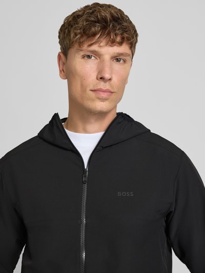Mężczyzna nosi kurtkę treningową Regular Fit Trainingsjacke mit Kapuze model 'LW_COMMUTERPRO' od BOSS Green, zbliżenie na górną część ciała.