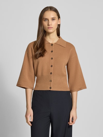 Frauenmodel trägt Strickjacke aus Viskose-Mix Modell 'SHYLA' von Noisy May in Braun mit Umlegekragen, 3/4-Arm, gerippten Abschlüssen, lockerer Passform, durchgehender Knopfleiste, Ganzkörperansicht von vorne.