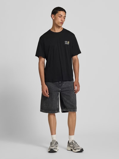 Männermodel trägt T-shirt met motiefprint model 'VINTAGE CARTOON' van Jack & Jones, puur katoen, regular fit, ronde hals, ruglengte bij maat M 69 cm, zwart met licht motief, ganzlichaamsaanzicht van voren.