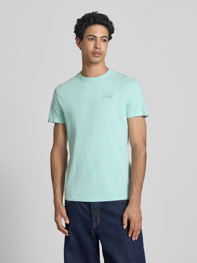 Männermodel trägt Regular Fit T-Shirt mit Logo-Stitching von Superdry in Hellgrün, reine Baumwolle, Rundhalsausschnitt, Ganzkörperansicht von vorne.