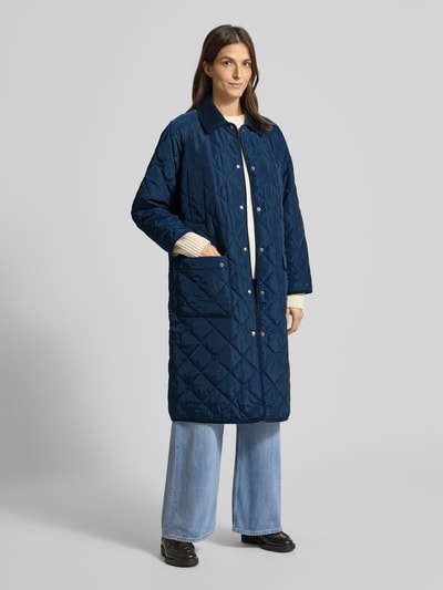 Vrouwenmodel draagt Regular Fit Steppmantel met Logo-Details van Tommy Hilfiger in effen donkerblauw met cordkraag, opgestikte zakken, lange mouwen en paspelafwerking, Ganzkörperansicht von vorne.