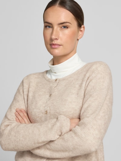 Vrouwenmodel draagt Regular fit gebreid jack uit mix van wol en alpaca model 'Almine' van MOS MOSH, beige, knoopsluiting, lange mouw, merkembleem, ruglengte maat S 51 cm, mouwlengte maat S 63 cm, close-up bovenlichaam.