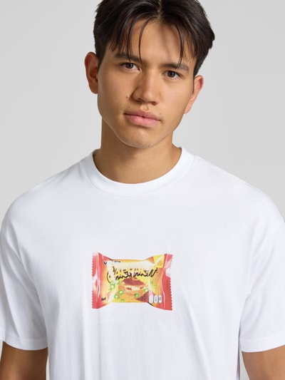 Męski model nosi Regular Fit T-Shirt mit Motiv-Print Model 'Road Side Snack' von Carhartt Work In Progress, biała bawełna, okrągły dekolt, nadruk z motywem, Długość tyłu w rozmiarze M: 72 cm, całkowite ujęcie górnej części ciała z przodu.