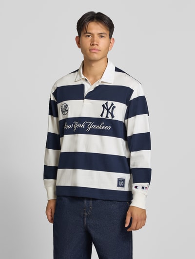 Männermodel trägt Relaxed Fit Poloshirt aus reiner Baumwolle von Champion mit breiten weißen und dunkelblauen Streifen, Statement-Stitching, Polokragen und langen Ärmeln, Ganzkörperansicht von vorne.