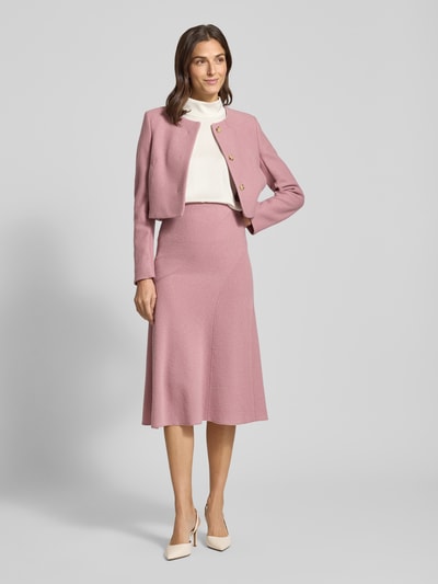 Frauenmodel trägt Boxy Fit Kurzblazer aus reiner Schurwolle Modell 'JICENA' von BOSS w kolorze różowym, gładka tekstura, długi rękaw, okrągły dekolt, boczne kieszenie, ukryte guziki, widoczne prążkowane wykończenie przy rękawie, wełniany materiał, Ganzkörperansicht von vorne.