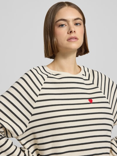 Frauenmodel trägt Oversized Sweatshirt aus Baumwoll-Mix Modell 'GRETA' von Pieces, cremefarben mit schwarzen Streifen, Label Stitching, Nahaufnahme Oberkörper.