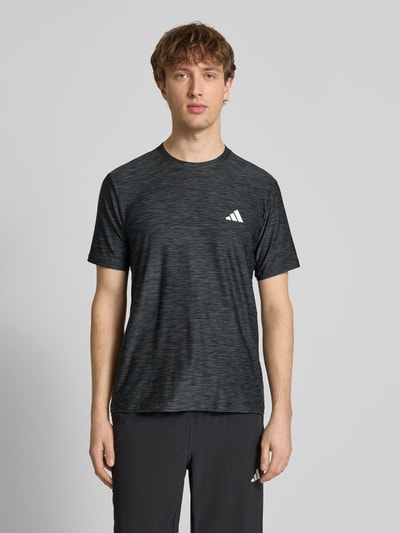 Männermodel trägt T-Shirt mit Label-Print von adidas Training in Schwarz mit dezentem Muster, Regular Fit, Nahaufnahme Oberkörper.
