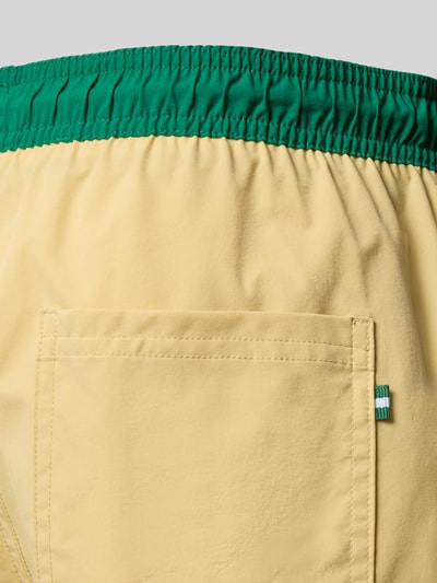 Frauenmodel trägt Badeshorts mit Gesäßtasche Modell 'MAUI' von JACK & JONES in Gelb mit grünem Bund, Label-Detail, Logo-Print, Detailaufnahme.
