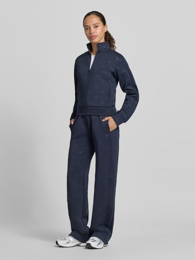 Frauenmodel trägt Wide Fit Sweatpants mit Allover-Logo-Print Modell 'Calista' von Guess Activewear in Dunkelblau, Ganzkörperansicht von vorne.