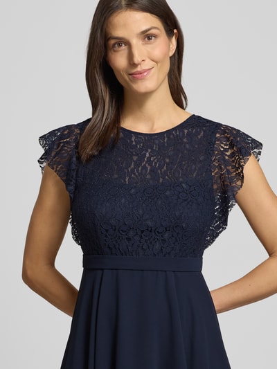 Frauenmodel trägt Knielanges Cocktailkleid mit Rundhalsausschnitt von Jake*s Cocktail in Dunkelblau, tailliert, blickdicht, Nahaufnahme Oberkörper.