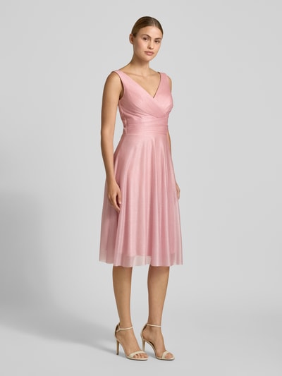 Frauenmodel trägt Knielanges Cocktailkleid mit V-Ausschnitt von TROYDEN COLLECTION, rosa Chiffon, taillierter Schnitt, breite Träger, Ganzkörperansicht von vorne.