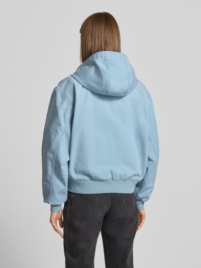 Frauenmodel trägt Sweatjacke mit Kapuze und Känguru-Tasche von Carhartt Work In Progress in Hellblau, Relaxed-Fit aus Reine Baumwolle, grobe Textur, Label-Detail, Rückenlänge 59 cm, Schulterbreite 52 cm, Brustweite 58 cm, Ärmellänge 60 cm, Ganzkörperansicht Rückansicht.