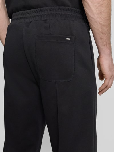 Männermodel trägt Regular Fit Spodnie dresowe aus mieszanka bawełny Model 'DINETO' von HUGO, efekt: jednolity kolor, naszywka z logo, kanty, elastyczny ściągacz z tunelem, wpuszczane kieszenie, kieszeń z tyłu, dzianina dresowa, widok z tyłu zbliżenie na kieszeń.