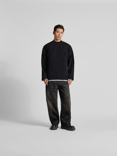 Männermodel trägt Regular Fit Sweatshirt aus Baumwolle von VETEMENTS in Schwarz mit Stehkragen und Statement-Stitching, langärmelig, Rückenlänge bei Größe M 80 cm, Ganzkörperansicht von vorne.