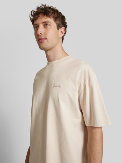 Męski model nosi Oversized T-Shirt mit Label-Stitching od Pegador, czysta bawełna, kolor jasny beż, krój oversize, okrągły dekolt, długość tyłu w rozmiarze M: 70 cm, półzbliżenie klatki piersiowej, widok z przodu.
