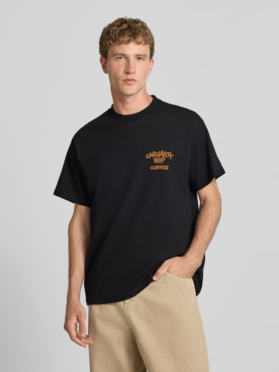 Männermodel trägt Regular Fit T-Shirt mit Motiv-Print auf der Rückseite von Carhartt Work In Progress, schwarze Baumwolle, Nahaufnahme Oberkörper.