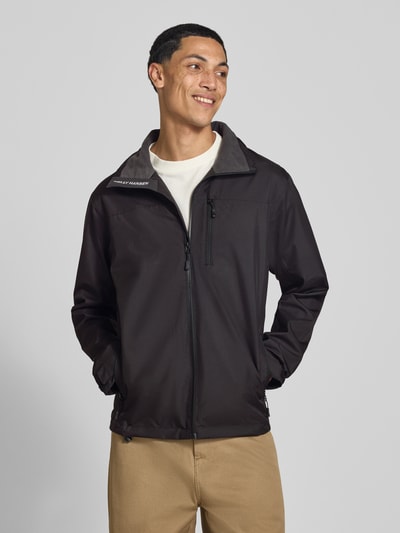Männermodel trägt Regular Fit Jacke mit Stehkragen Modell 'Crew' von Helly Hansen in Schwarz, Logo-Print, Reißverschlusstaschen, Ganzkörperansicht von vorne. Herren Jacke, Stehkragen, Napoleontasche, Rückenlänge 73 cm, Schulterbreite 48 cm, Brustweite 56 cm, Ärmellänge 68 cm.