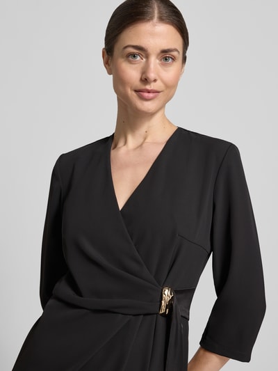 Modelka prezentuje knielanges Cocktailkleid in Wickel-Optik von Rinascimento, czarny kolor, mieszanka materiałów z dodatkiem streczu, prosty krój, długość do kolan, rękaw o dł. 3/4, szerokość w rozmiarze S: 46 cm, długość tyłu w rozmiarze S: 90 cm, długość rękawa w rozmiarze S: 44 cm, zapięcie kopertowe, gładka tekstura, zbliżenie na górną część ciała