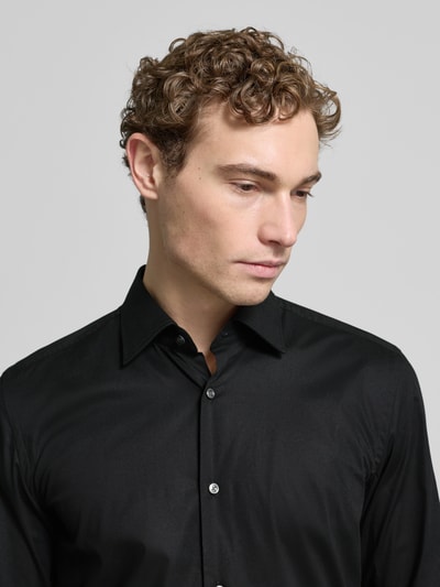 Męski model nosi Slim Fit Businesshemd aus Popeline mit Stretch-Anteil od BOSS, czarna mieszanka bawełny i elastanu, krój slim fit, kołnierzyk typu kent, na całej długości listwa guzikowa, sportowe mankiety, zaokrąglony dół, łatwa pielęgnacja, długość tyłu 76 cm, szerokość ramion 47 cm, długość rękawów 67 cm, popelina, łatwa w pielęgnacji, kolor czarny, gładka tekstura, widok: zbliżenie na górną część ciała.