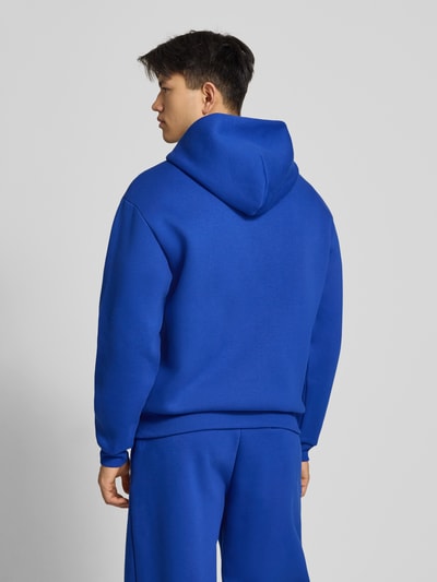 Männermodel trägt blaue Sweatjacke mit Känguru-Tasche von REVIEW aus Baumwoll-Mix, Relaxed-Fit, Rückenansicht, Ganzkörperansicht.