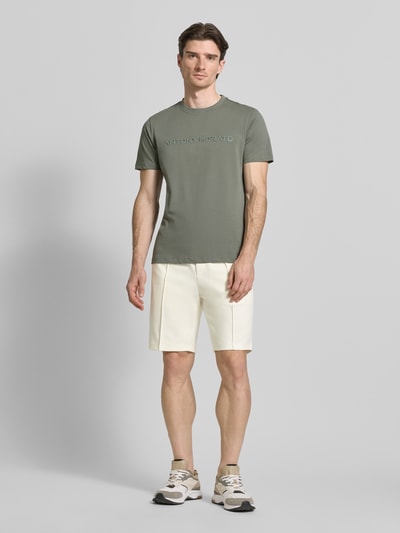 Męski model nosi Regular Fit Shorts mit Tunnelzug od Antony Morato, kolor ecru, bawełna, elastyczny pas i tunelem, szerokość w rozmiarze M 41 cm, długość nogawki 25 cm, widok całej sylwetki z przodu.