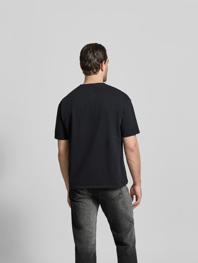 Männermodel trägt Regular Fit T-Shirt mit Logo-Print von RHUDE, reine Baumwolle, Rundhalsausschnitt, kurzärmelig, Rückenlänge 68 cm, Ganzkörperansicht Rückansicht.
