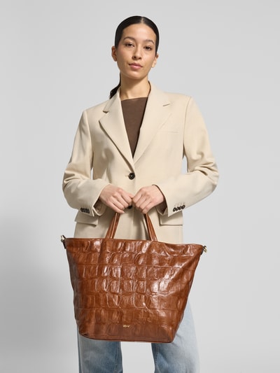 Frauenmodel trägt Tote Bag mit Logo-Detail Modell 'Alba' von Abro, strukturierte braune Oberfläche, Reißverschluss, Ganzkörperansicht von vorne.