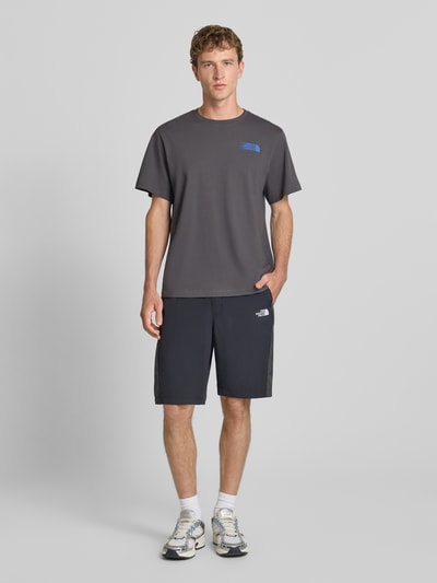 Männermodel trägt Relaxed Fit T-Shirt mit Logo-Print von The North Face in Dunkelgrau, reine Baumwolle, Rundhalsausschnitt, Ganzkörperansicht von vorne.