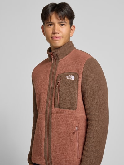 Männermodel trägt Fleecejacke mit Stehkragen Modell 'YUMIORI' von The North Face in Braun, lockere Passform, Nahaufnahme Oberkörper. Rückenlänge 71 cm, Ärmellänge 71 cm, seitliche Reißverschlusstaschen, Napoleontasche, elastische Abschlüsse.