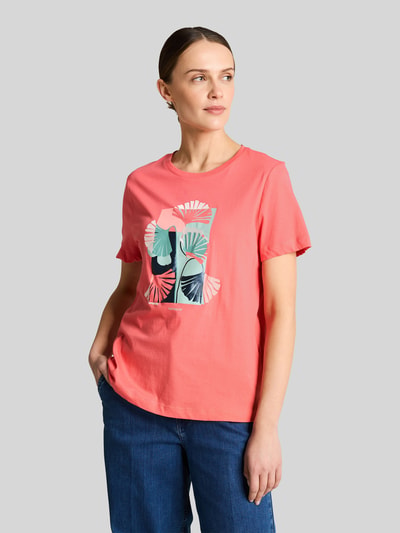 Frauenmodel trägt Regular Fit T-Shirt aus reiner Baumwolle von Tom Tailor, Optik: Unifarben, Label-Print, Motiv-Print-Stitching, Rundhals, Kurzarm, Rumpfabschluss mit Seitenschlitzen, Materialverarbeitung: Jersey, Motiv in Rosa, Grün und Blau, glatte Struktur, Damen T-Shirt, Ganzkörperansicht von vorne.