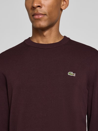 Männermodel trägt bordeauxfarbenen Regular Fit Pullover aus Baumwoll-Mix von Lacoste, strukturierte Oberfläche, Nahaufnahme Oberkörper. Herren Pullover von Lacoste