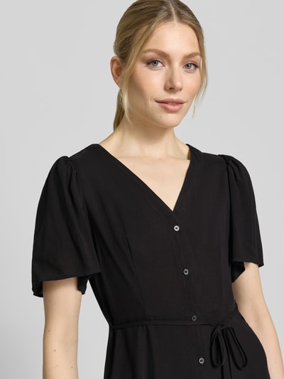 Frauenmodel trägt Leicht ausgestelltes Minikleid aus reiner Viskose Modell 'ALBA' von Vero Moda, Optik: Unifarben, Passform: Leicht ausgestellt, Mini-Länge, Ausschnitt: V-Ausschnitt, Details: Taillengürtel, Verschluss: Knopfleiste, Ärmelform: Kurzarm, Material: Reine Viskose, Stoff wirkt weich, Nahaufnahme Oberkörper.