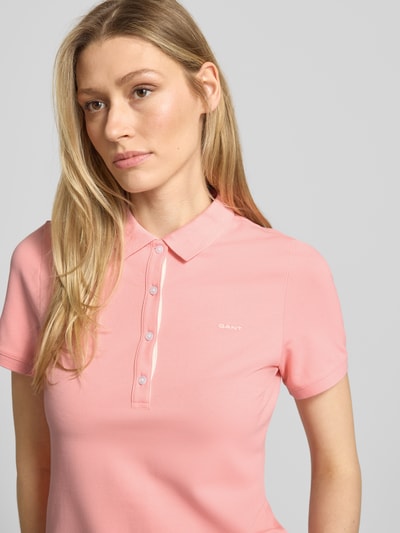 Vrouwenmodel draagt Slim Fit Poloshirt met Label-Stitching van Gant in mix van katoen en elastaan, slim fit, knoopsluiting, ruglengte maat S 59 cm, detailopname bovenlichaam.