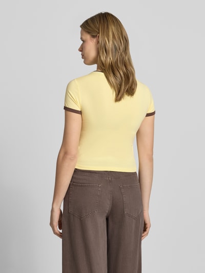 Frauenmodel trägt Slim Fit T-Shirt mit Statement-Print Modell 'Molly' von Noisy May in Gelb-Braun, elastischer Baumwoll-Mix, Ganzkörperansicht Rückansicht.