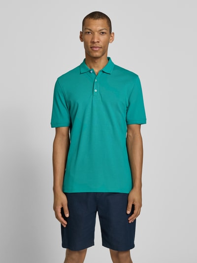 Mężczyzna nosi Slim Fit Poloshirt aus Baumwoll-Mix Modell 'Pete' von Brax w kolorze zielonym, kołnierzyk polo, krój slim fit, mieszanka bawełny, długość tyłu w rozmiarze M 71 cm, Ganzkörperansicht von vorne.