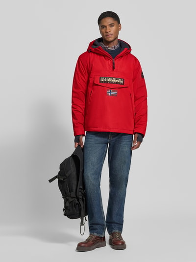 Männermodel trägt Jacke mit Kapuze und kurzem Reißverschluss von Napapijri in Rot, Label-Patches, Kängurutasche, Ganzkörperansicht von vorne, gerader Schnitt, Modell RAINFOREST NEXT