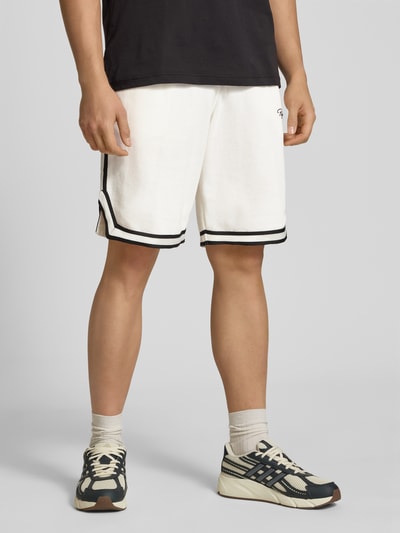 Męski model nosi Shorts mit Logo-Stitching Modell 'Signar' od Pegador, białe z czarnymi paskami, czysta bawełna, krój regular fit, elastyczny pas, szerokość w rozmiarze M: 40 cm, długość nogawki: 27 cm, widok całej sylwetki z przodu.