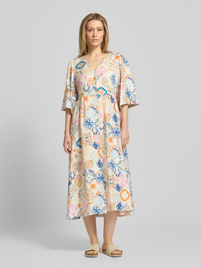 Frauenmodel trägt Tunikakleid aus Viskose-Mix mit Leinen-Viskose-Anteil Modell 'LANCIE' von ICHI, Allover-Look, A-Linie, V-Ausschnitt, Knopfleiste, Midikleid, sanfte Beige-Nuance mit buntem Muster, weiche Textur, Ganzkörperansicht von vorne.