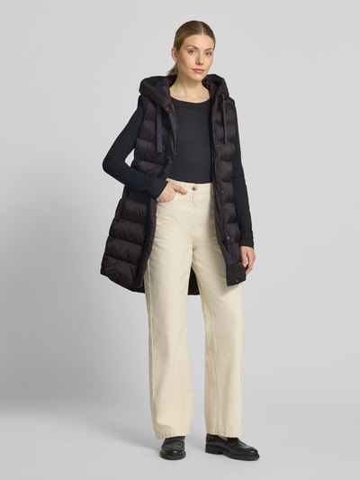 Vrouwenmodel draagt Regular Fit bodywarmer in stiksels van FUCHS SCHMITT, zwart, met capuchon en steekzakken met ritssluiting, ruglengte 77 cm, schouderbreedte 41 cm, borstwijdte 51 cm, ganzekijk van voren.