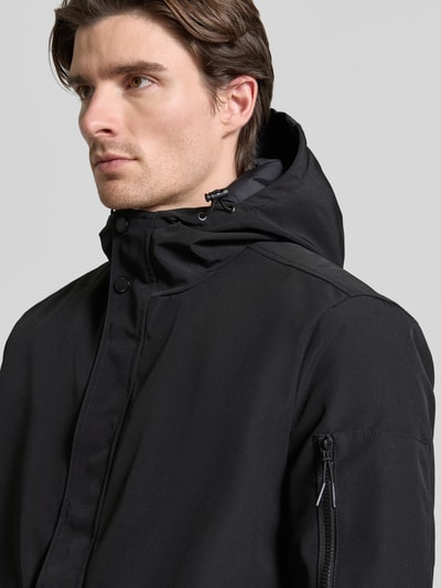Männermodel trägt Jacke mit Kapuze von MCNEAL in Schwarz mit verdecktem Reißverschluss, Pattentaschen, Reißverschlusstasche am Ärmel. Nahaufnahme Oberkörper. Rückenlänge 99 cm, Schulterbreite 48 cm, Brustweite 62 cm, Ärmellänge 67 cm, Regular Fit.