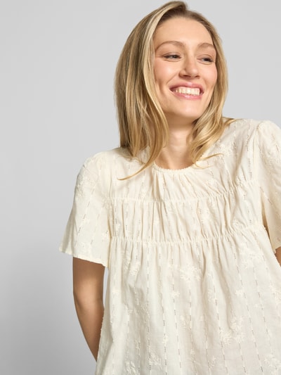Modelka kobieca nosi Blusenshirt mit Stitchings Modell 'LANA' od ICHI, mieszanka bawełny i wiskozy, krój regular fit, jasny kolor, teksturowana tkanina z przeszyciami, okrągły dekolt, długość tyłu 54 cm w rozmiarze 36, długość rękawa 25 cm w rozmiarze 36, zbliżenie na górną część ciała z przodu.