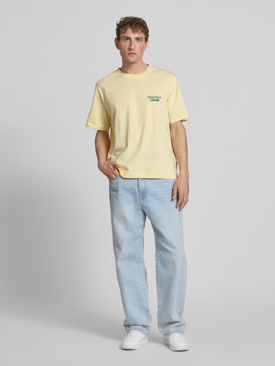 Männermodel trägt T-Shirt mit Label-Print von Jack & Jones in Gelb, Reine Baumwolle, Relaxed-Fit, Rundhalsausschnitt, Ganzkörperansicht von vorne.