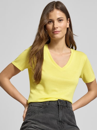Frauenmodel trägt Regular Fit T-Shirt aus Viskose-Mix von LIU JO SPORT in Gelb mit V-Ausschnitt, Glitzer-Optik, Logo-Detail, Nahaufnahme Oberkörper.