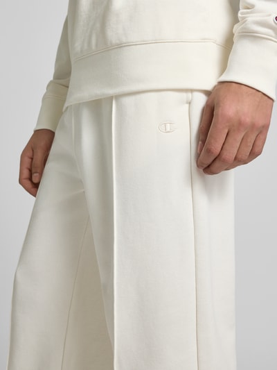 Männermodel trägt Sweatpants mit Längsnähten und Label-Stitching von CHAMPION aus Baumwoll-Mix in Creme, Nahaufnahme Oberschenkel.